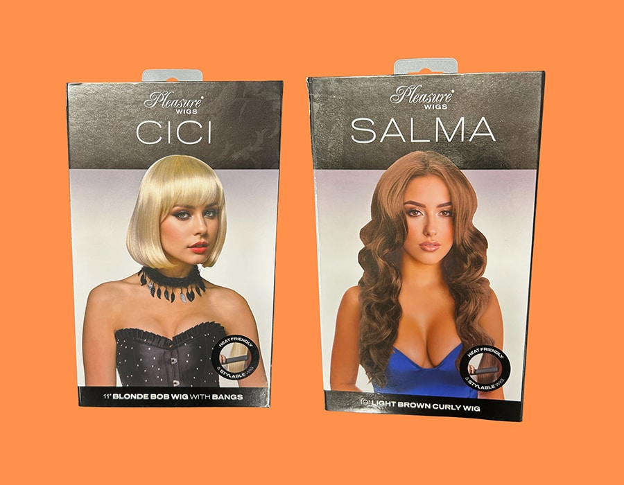 Two Pleasure Wigs product boxes: one featuring a blonde bob wig named Cici, and one featuring a long light brown curly wig named Salma.